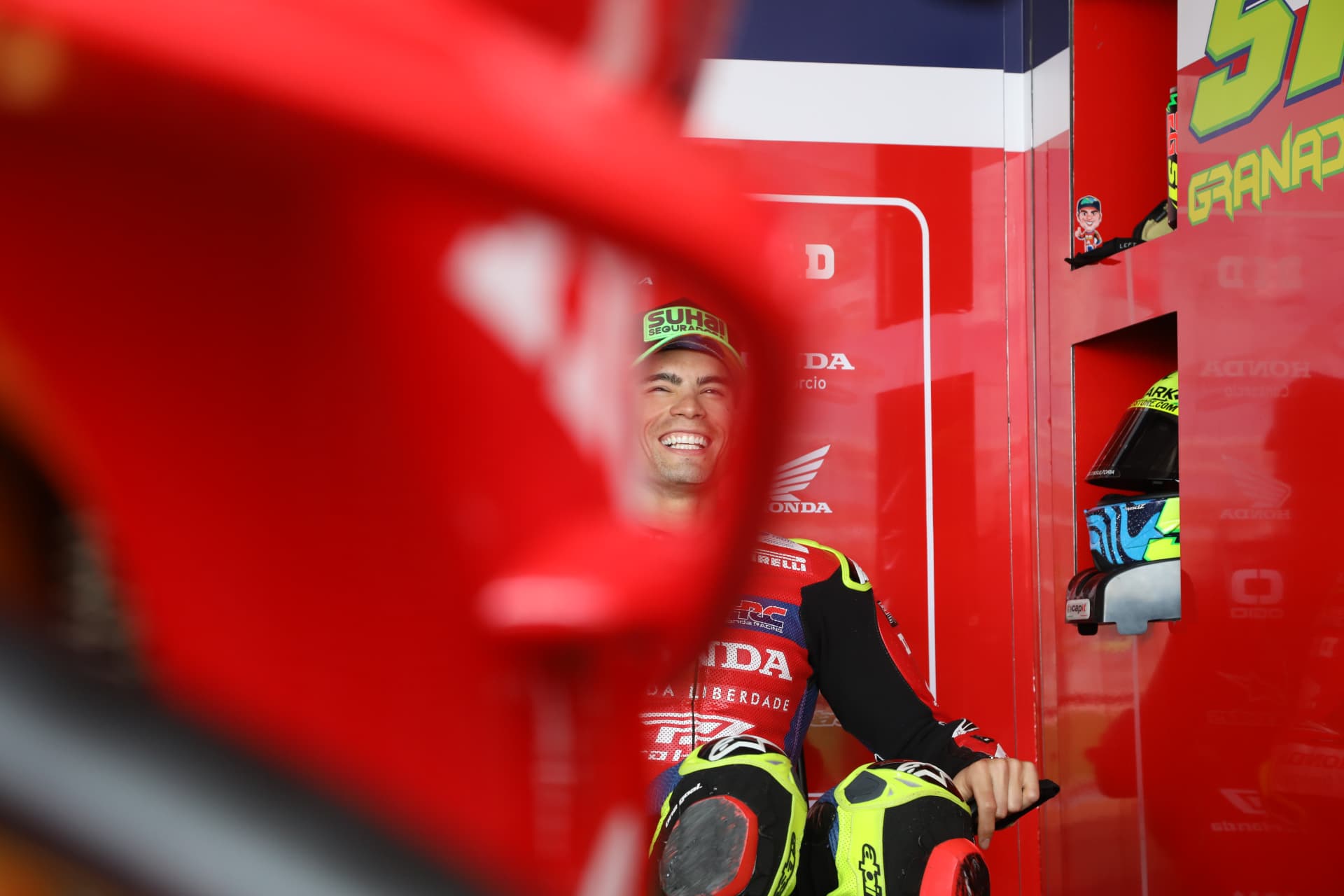Honda rider laughing in the garage, seen through a red bodywork panel
