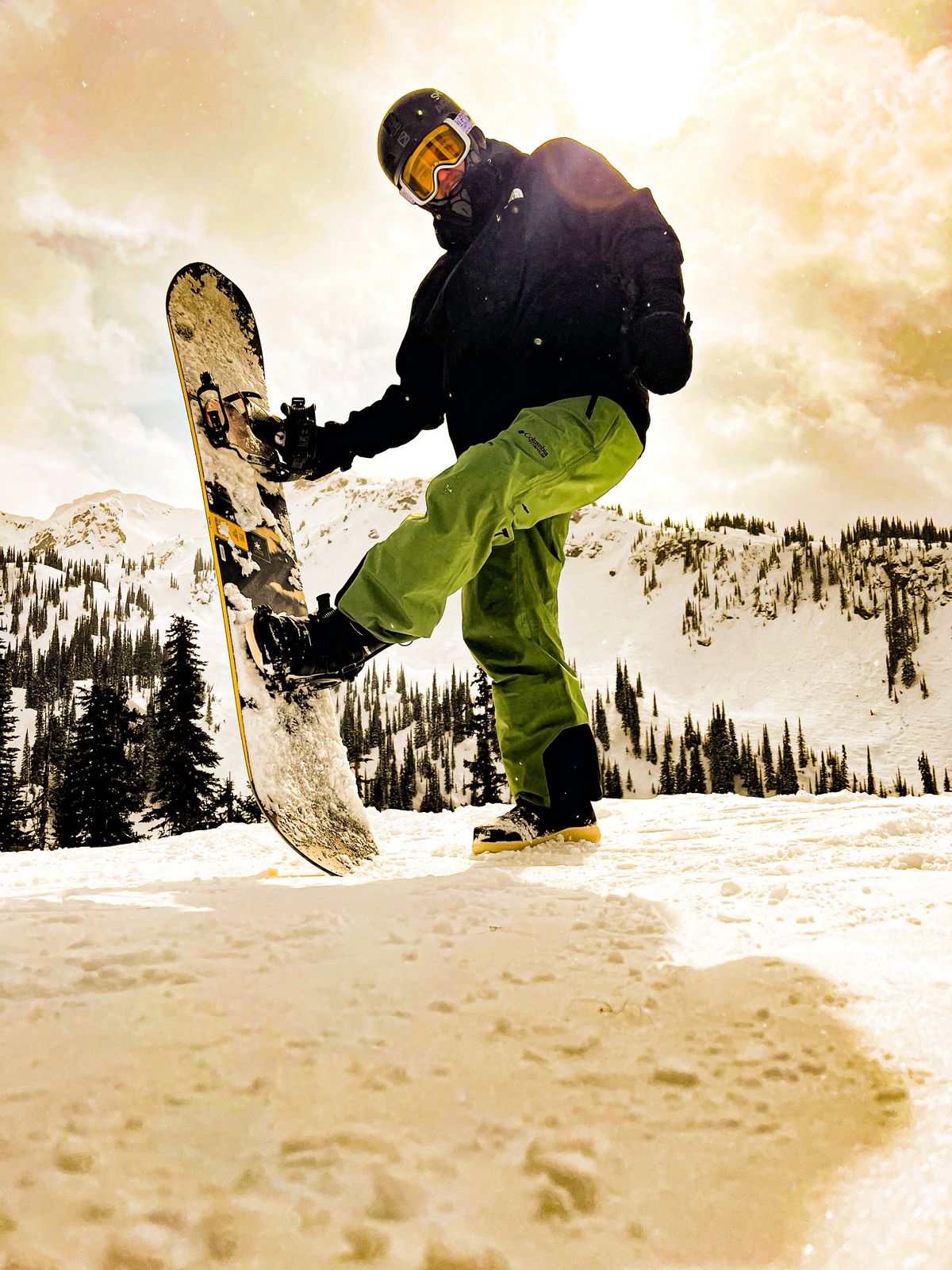 Snowboarder standing with his board on a sunlit mountain ridge