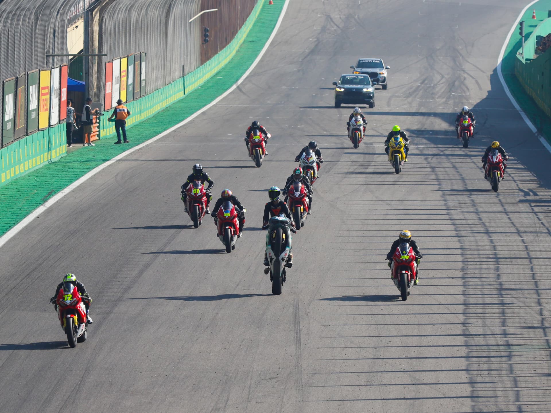 Field of superbikes racing behind the safety car