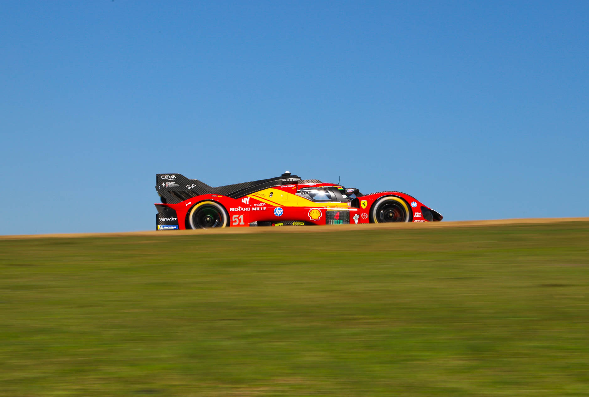 Ferrari 499P number 51 cresting the hill against a clear blue sky