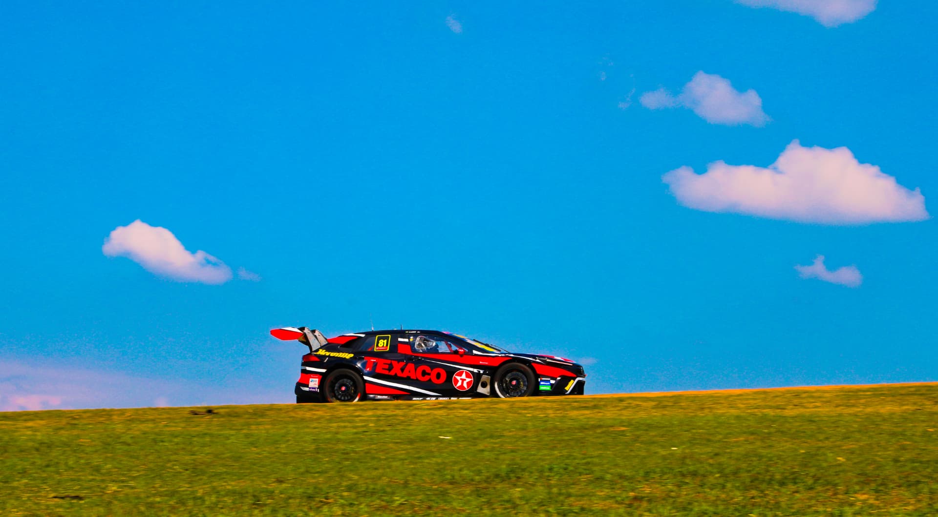Texaco liveried stock car cresting the hill against a blue sky