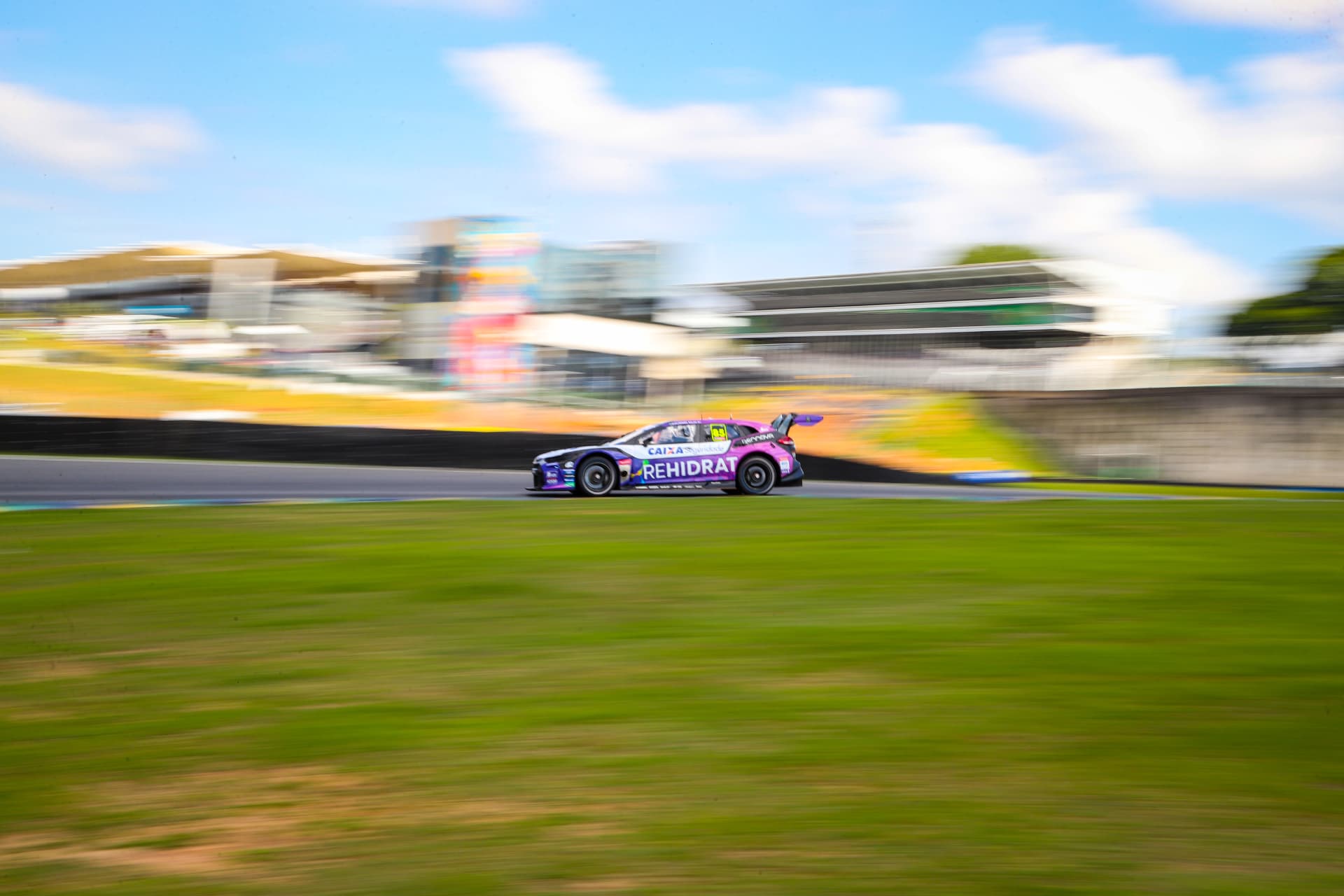 Purple and blue stock car blurring past the main straight grandstand